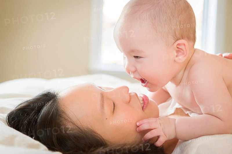 Young mixed-race chinese and caucasian baby boy laying in his bed with his mother