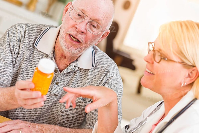 Doctor or nurse explaining prescription medicine to attentive senior man