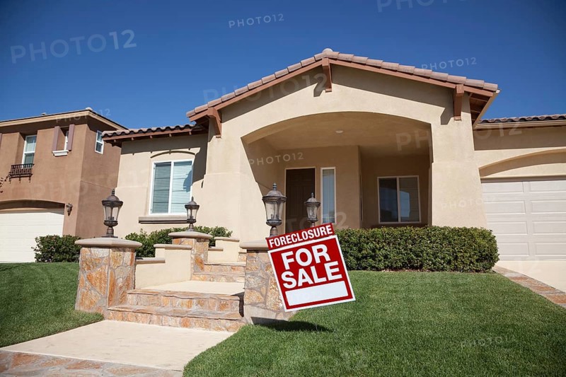 Foreclosure home for sale sign and house with dramatic sky background