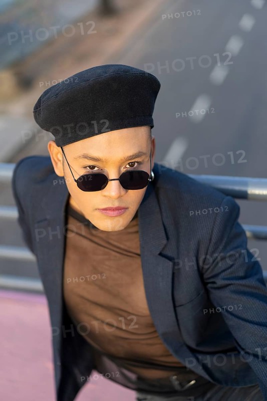 Latino gay male with makeup wearing trendy hat posing on a bridge