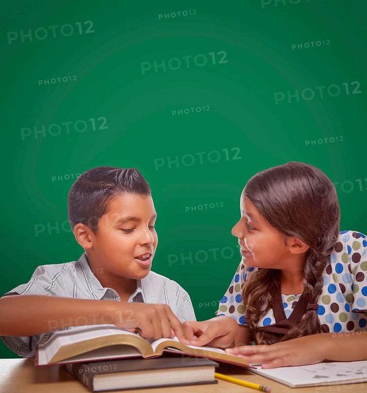 Blank chalk board behind hispanic boy and girl having fun studying together