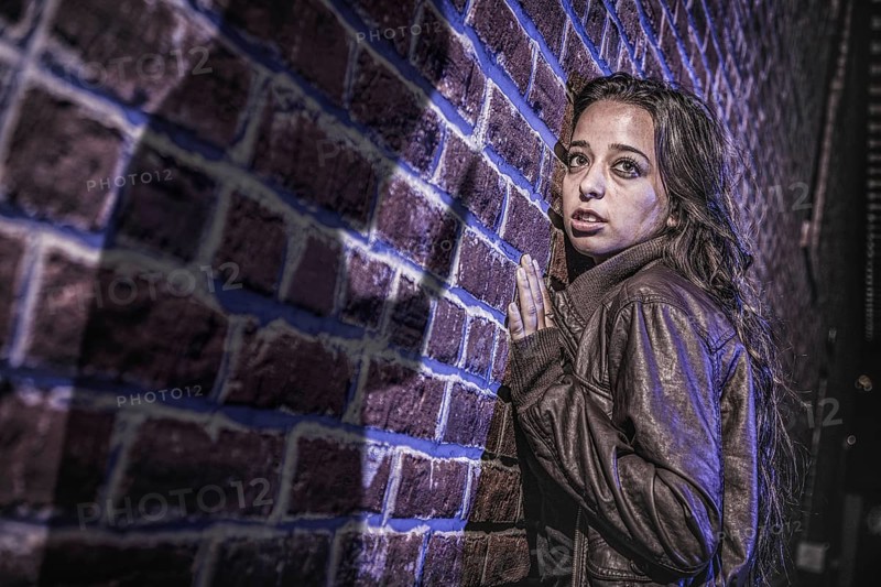 Male shadow figure with knife threatens frightened young woman against brick wall