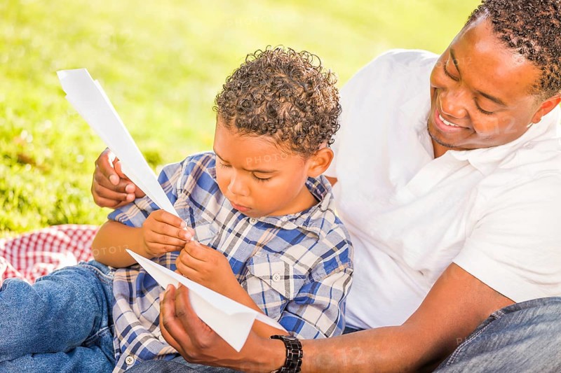 Happy african american father and mixed-race son playing with paper airplanes in the park
