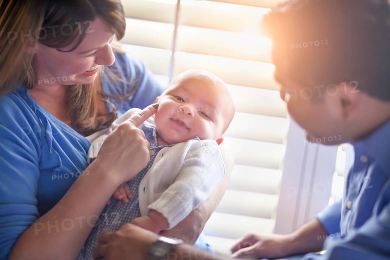 Happy mixed-race couple enjoying their newborn son in the light of the window