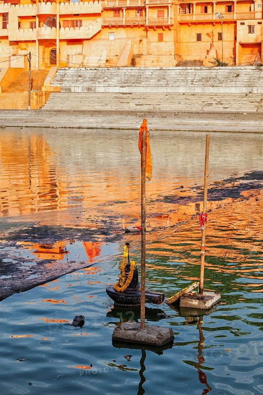 Lingam religious symbol representation of the Hindu deity Shiva decorated with flower garland used for worship in Kshipra river