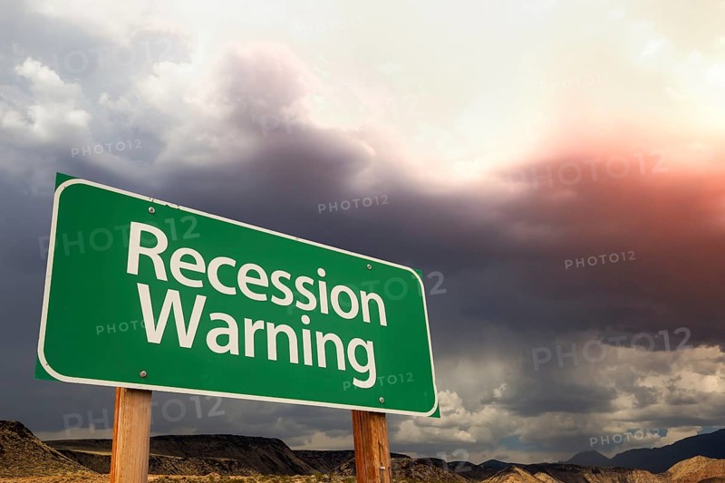 Recession warning green road sign over dramatic clouds and sky