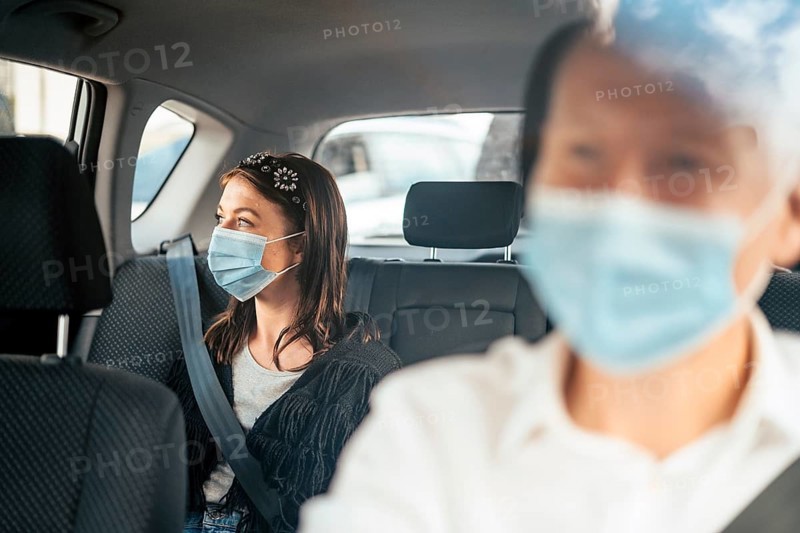 A woman wearing a protective mask sitting on the back seat of a taxi car