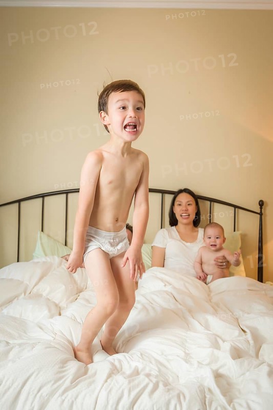 Young mixed-race chinese and caucasian boy jumping in bed with his family