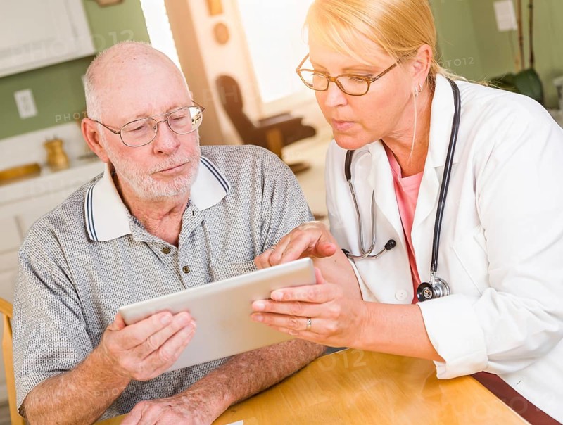 Female doctor or nurse showing senior man touch pad computer at home