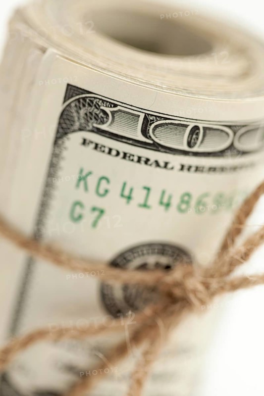 Roll of one hundred dollar bills tied in burlap string on white