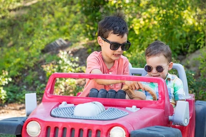 Young mixed-race chinese and caucasian brothers wearing sunglasses playing in toy car