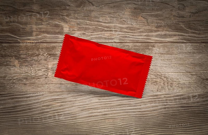 Blank red condiment packet floating on aged wood background