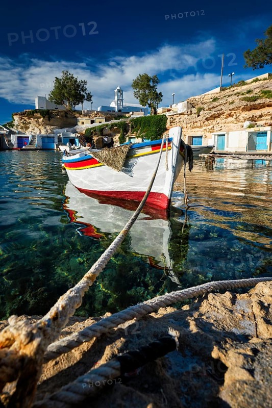 Fishing boats moored in crystal clear turquoise sea water in harbour in Greek fishing village of Mandrakia