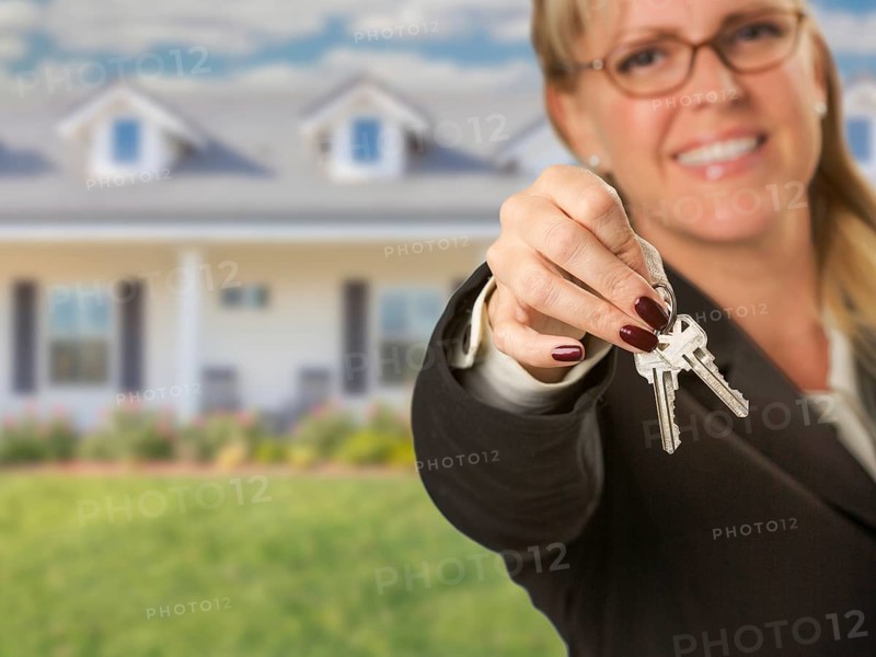 Real estate agent handing over new house keys with house behind