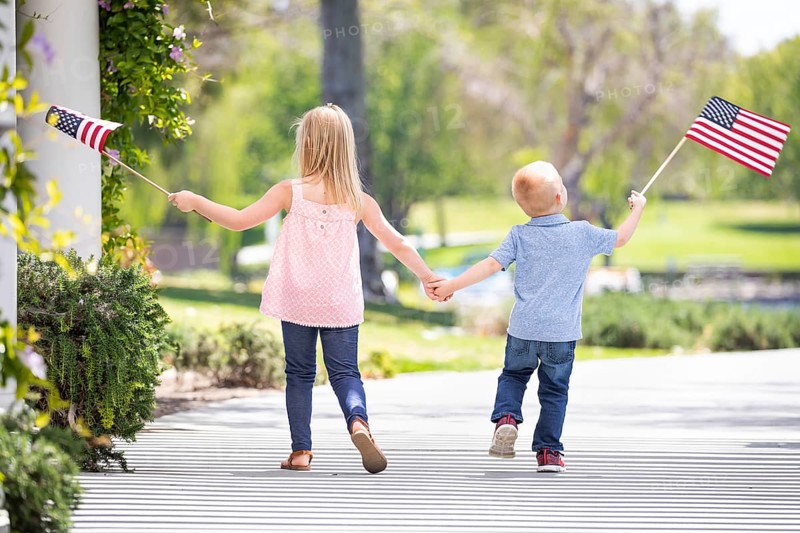 Young sister and brother holding hands and waving american flags at the park