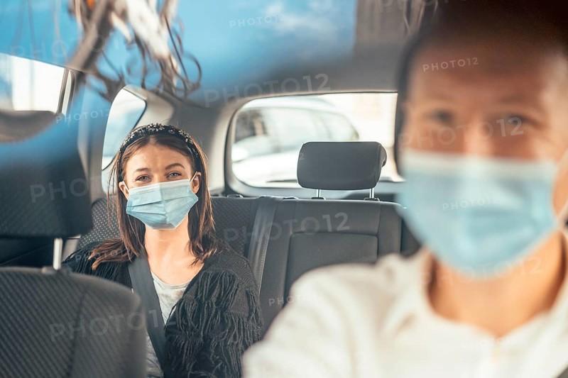 A woman wearing a protective mask sitting on the back seat of a taxi car