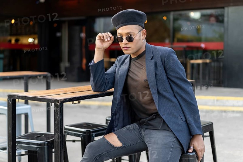 Latin gay male with makeup wearing fashion hat posing in the street