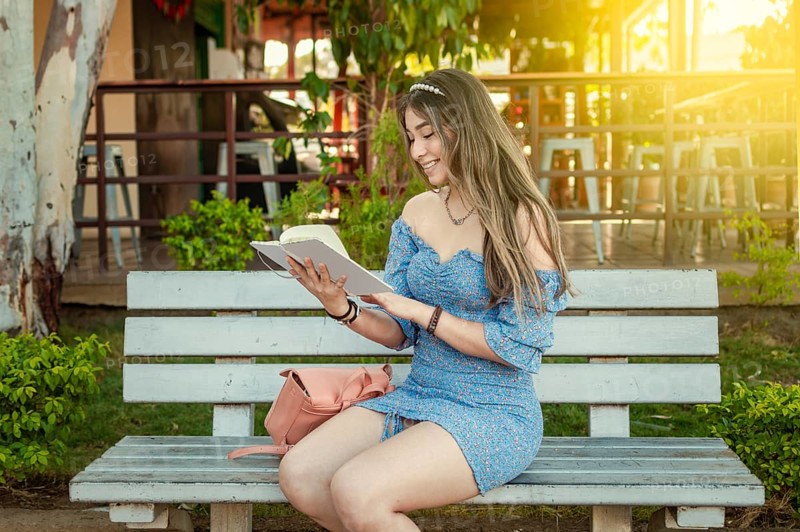 A cute girl sitting on a bench reading a book