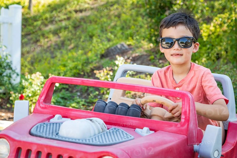 Young mixed-race chinese and caucasian boy wearing sunglasses playing in toy car