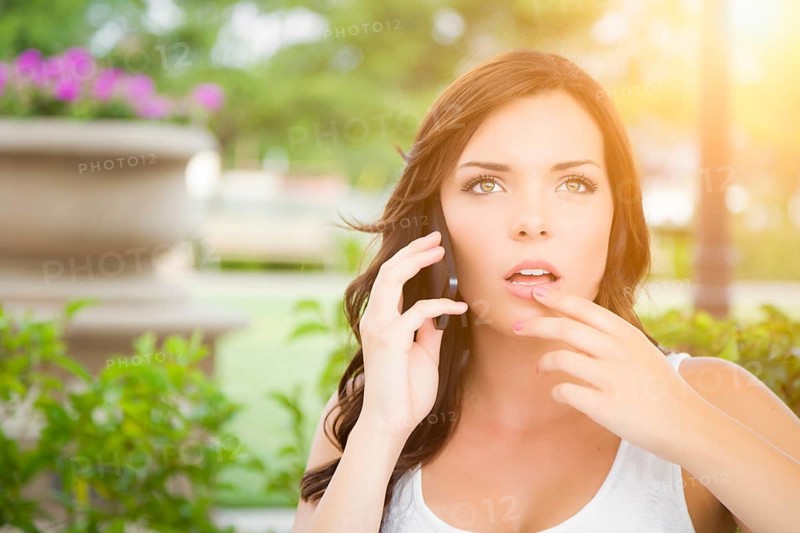 Shocked young adult female talking on cell phone outdoors on bench