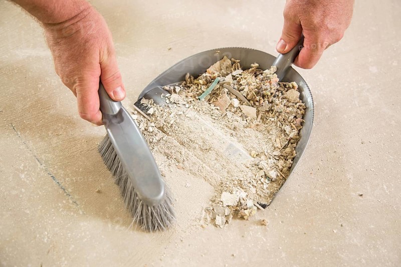 Worker picking up pile of debris on cement with brush and dust pan