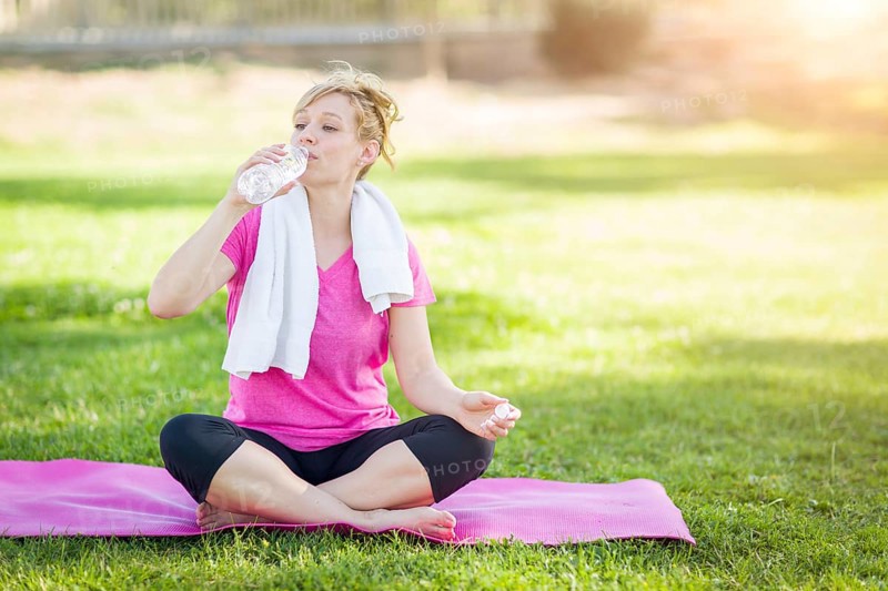 Young fit adult woman outdoors on her yoga mat with towel drinking from her water bottle