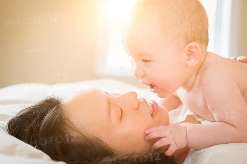 Young mixed-race chinese and caucasian baby boy laying in his bed with his mother