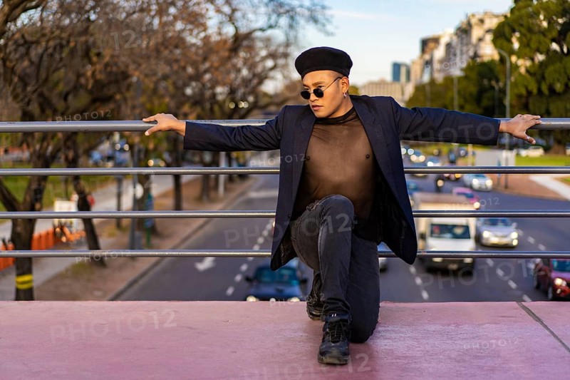 Latino gay male with makeup wearing trendy hat posing on a bridge