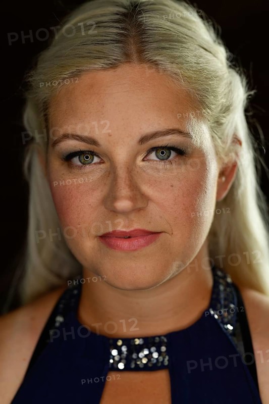 Portrait im Studio mit schwarzem Hintergrund von vorne einer jungen huebschen Frau mit langen blonden Haaren. Die Sommersprossen und die roten Lippen passen zu den blauen Augen