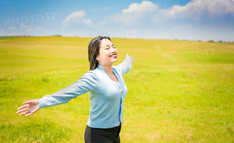 Young woman smiling and spreading her hands in the green field
