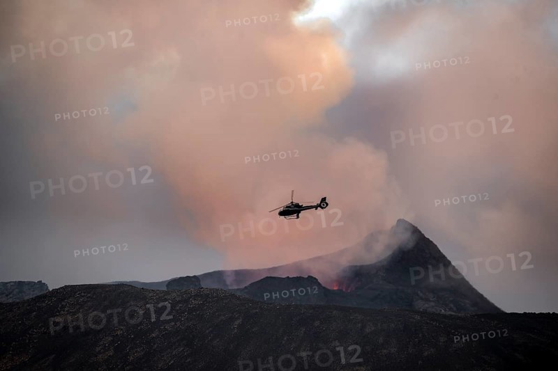 Helicopter flying over smoking active volcanic crater