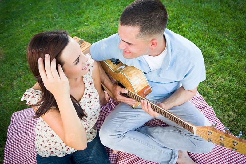 Young adult man playing guitar for his girlfriend in the park