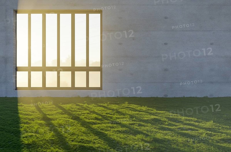 Window with bright sun light shining through concrete wall in grass and rocks field