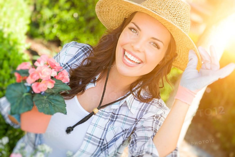 Happy young adult woman wearing hat and gloves gardening outdoors