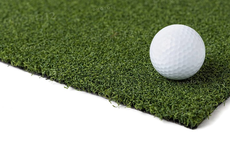Golf ball resting on section of artificial turf grass on white background