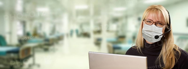 Woman sitting at computer with phone headset within hospital