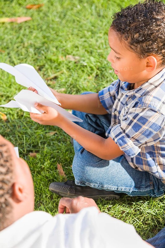 Happy african american father and mixed-race son playing with paper airplanes in the park