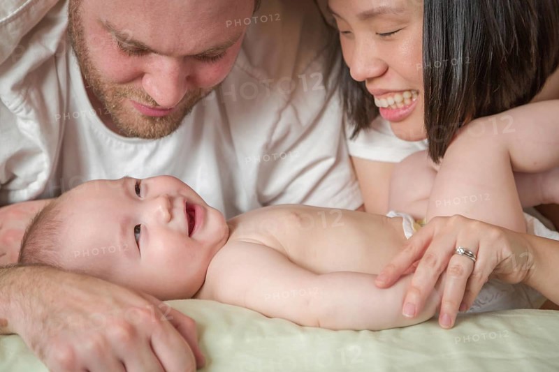 mixed-race chinese and caucasian baby boy laying in bed with his father and mother