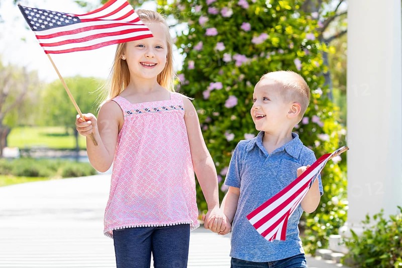 Young sister and brother waving american flags at the park