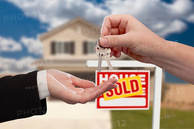 Handing over the house keys in front of real estate sign and sold new home