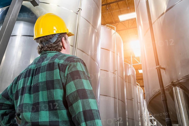 Man wearing hard hat looking up at large industrial tanks