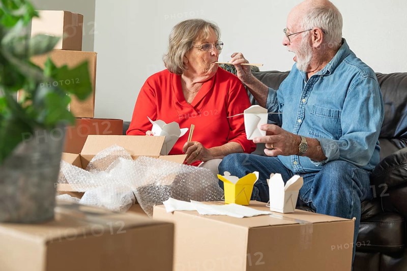 Senior couple enjoying chinese food surrounded by moving boxes