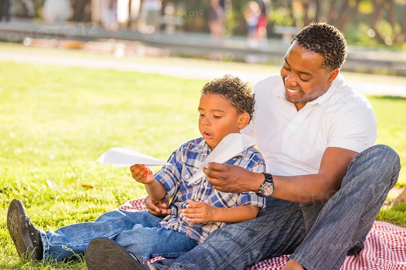 Happy african american father and mixed-race son playing with paper airplanes in the park