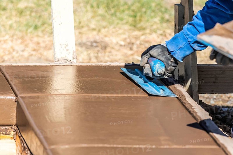Construction worker using trowel on wet cement forming coping around new pool