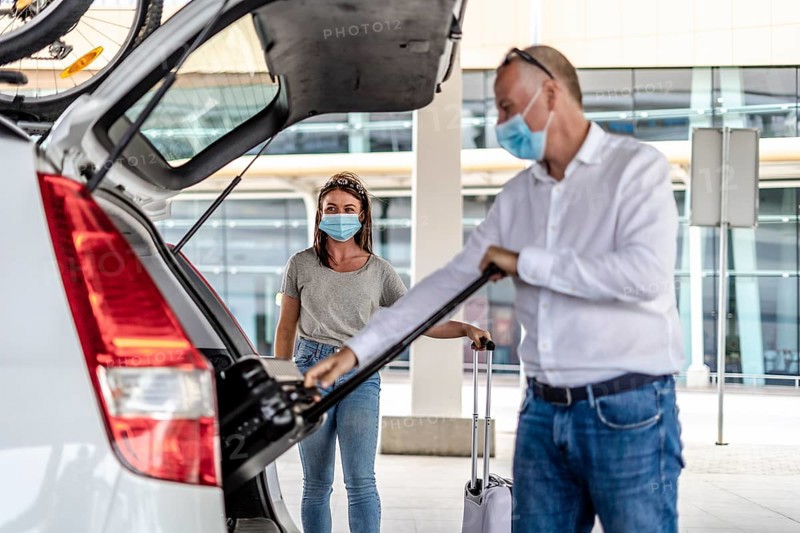 A taxi or Uber driver helping a passenger in a protective mask with her luggage at the airport