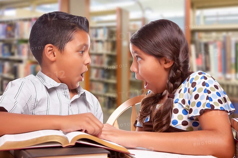 Hispanic boy and girl having fun studying together in the library