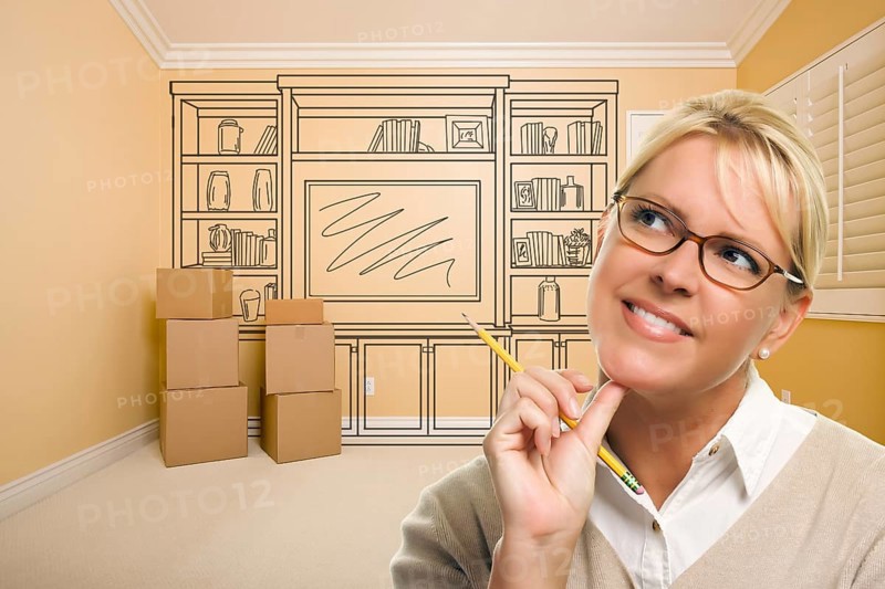 Daydreaming woman holding pencil in empty rom with built in shelf design drawing on wall