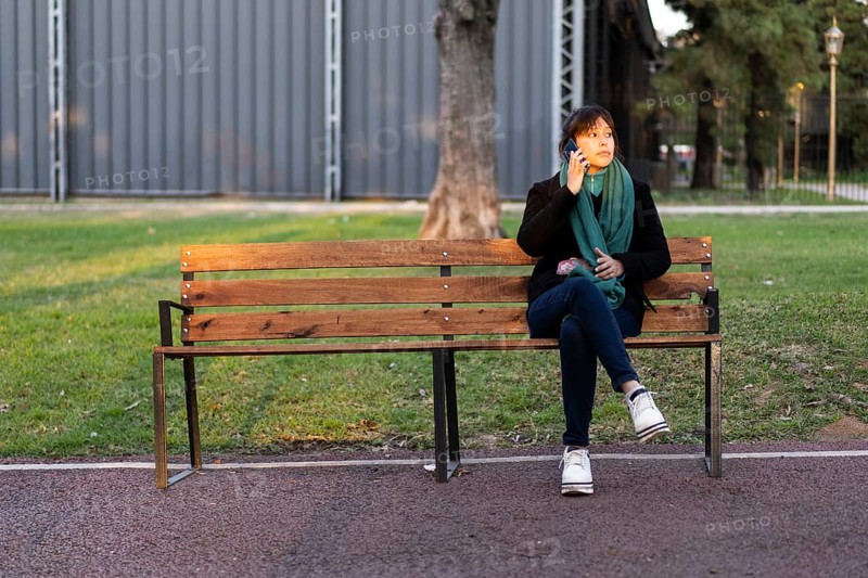 Latin woman sitting on a bench in a park talking on a cell phone