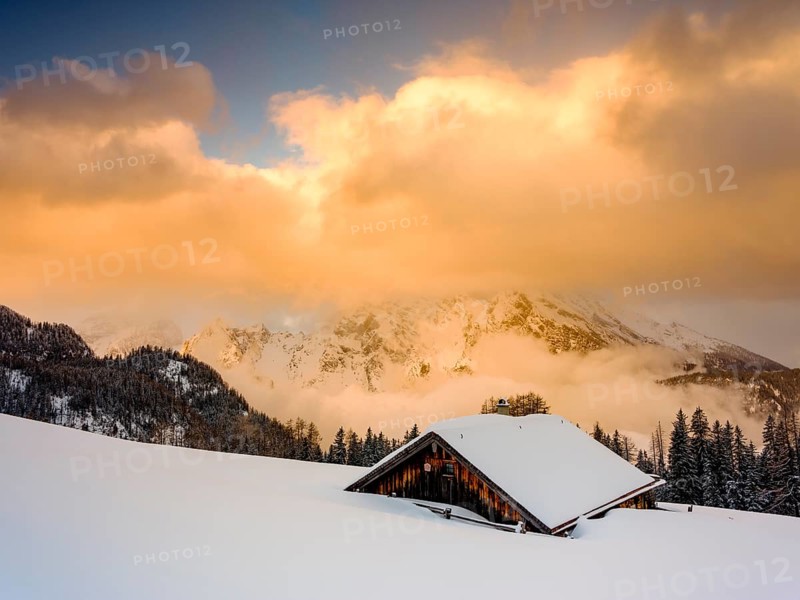 Snow-covered Priesbergalm in front of cloud-covered Watzmann