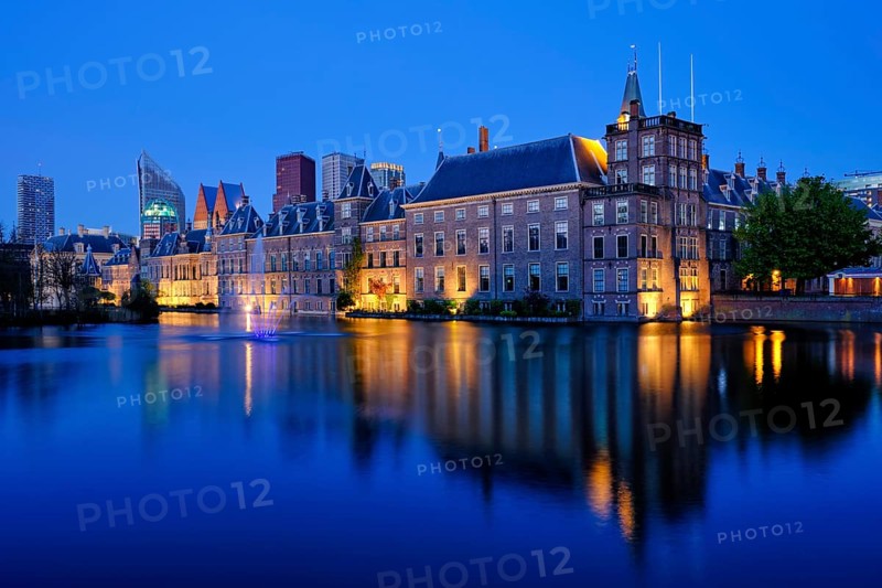 View of the Binnenhof House of Parliament and the Hofvijver lake with downtown skyscrapers in background illuminated in the evening. The Hague